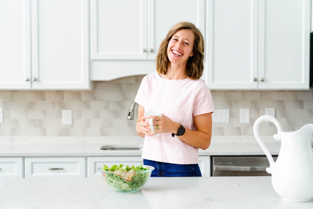 Woman in pink shirt in clean kitchen holding coffee cup