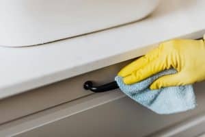 A professional cleaner wiping a dusty air vent in a modern apartment to improve indoor air quality.